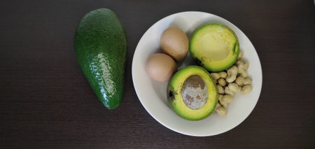 Avocado halved, boiled egg, and boiled peanuts Placed in a white plate, outside the plate, there was a large, shiny avocado fruit. All set on a black wooden floor. From the top view: It is usually eatの写真素材