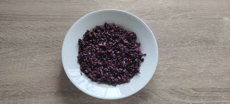 Riceberry rice in a white plate, placed on a wooden table : Dark purple rice similar to berries that is dark purple when ripe It is brown rice that will smell good. that is unique It also has an aromaの写真素材