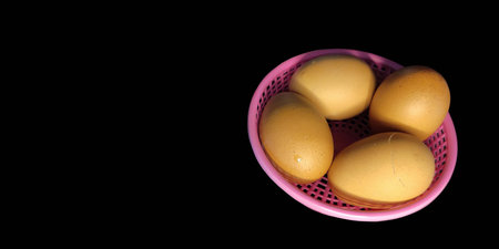 4 hard boiled ready-to-eat eggs, cracked, in a small pink basket, black background, top view.