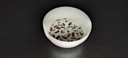Homemade red bean and mung bean dessert topped with bean milk It's a healthy little dessert. in a white bowl black background made of woodの写真素材