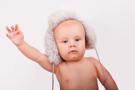 Portrait of cute caucasian baby nine month year old with blue eyes wearing a furry hat on a light background holding handの写真素材