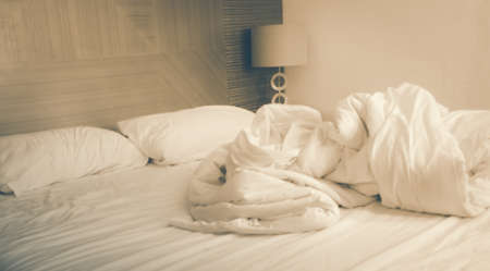 An blurred messy bed with white linens in Vintage tone.の写真素材