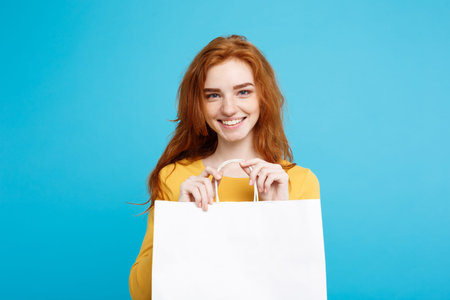 Close up Portrait young beautiful attractive redhair girl smiling with white shopping bag. Blue...