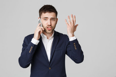 Business Concept - Portrait young handsome angry business man in suit talking on phone looking at camera. White background.の写真素材