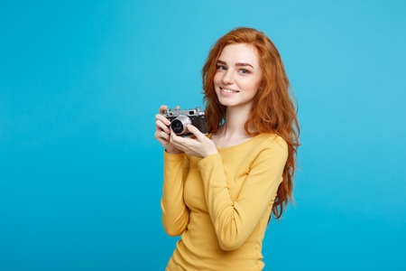 Close up Portrait young beautiful attractive ginger girl happy smiling with vintage camera and ready to travel. Blue Pastel Background. Copy space.の写真素材