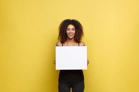 Business Concept - Close up Portrait young beautiful attractive African American smiling showing plain white blank sign. Yellow Pastel studio Background. Copy space.の写真素材