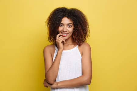 Beautiful attractive African American woman with curly afro hair thinking of something. Yellow studio background. Copy Space.の写真素材