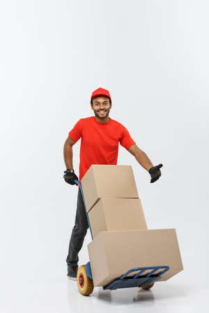 Delivery Concept - Portrait of Handsome African American delivery man or courier pushing hand truck with stack of boxes. Isolated on Grey studio Background. Copy Space.の写真素材