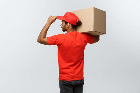 Delivery Concept - back view of Handsome African American delivery man with box package. Isolated on Grey studio Background. Copy Space.の写真素材