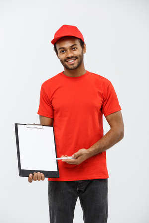 Delivery Concept - Portrait of Handsome African American delivery man or courier showing a confirmation document form to sign. Isolated on Grey studio Background. Copy Space.の写真素材