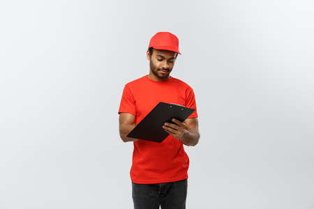 Delivery Concept - Portrait of Handsome African American delivery man or courier writing on a order document. Isolated on Grey studio Background. Copy Space.の写真素材