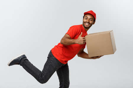 Delivery Concept - Handsome African American delivery man rush running for delivering a package for customer. Isolated on Grey studio Background. Copy Space.の写真素材