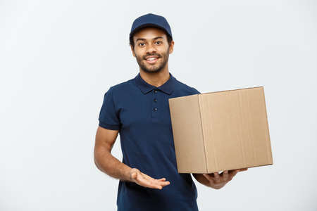 Delivery Concept - Portrait of Happy African American delivery man pointing hand to present a box package. Isolated on Grey studio Background. Copy Space.の写真素材