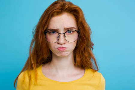 Headshot Portrait of tender redhead teenage girl with serious expression looking at camera. Caucasian woman model with ginger hair posing indoors.Pastel blue background. Copy Space.の写真素材