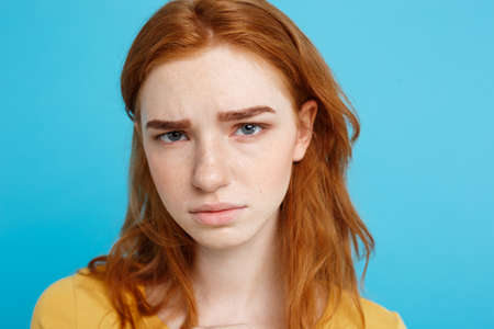 Headshot Portrait of tender redhead teenage girl with serious expression looking at camera. Caucasian woman model with ginger hair posing indoors.Pastel blue background. Copy Space.の写真素材