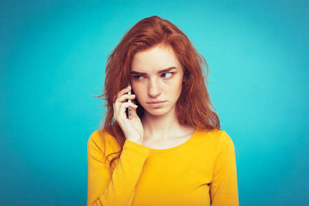 Lifestyle concept - Portrait of ginger red hair girl with shocking and stressful expression while talking with friend by mobile phone. Isolated on Blue Pastel Background. Copy space.の写真素材