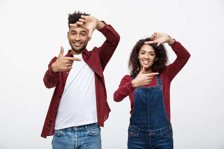 Happy young African American couple looking through a finger frame and smiling while standing isolated on white.の写真素材