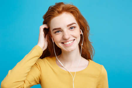 Lifestyle concept - Portrait of cheerful happy ginger red hair girl enjoy listening to music with headphones joyful smiling to camera. Isolated on Blue Pastel Background. Copy space.の写真素材