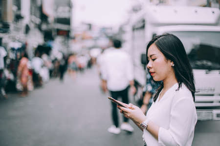 side view of a young woman playing mobile phone on the famous backpacker street Khao San in Bangkok, Thailandの写真素材