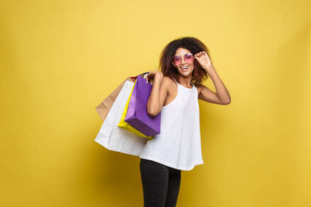 Shopping Concept - Close up Portrait young beautiful attractive African woman smiling and joyful with colorful shopping bag. Yellow Pastel wall Background. Copy Space.の写真素材