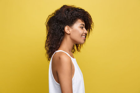 Side view portrait of beautiful attractive African American woman over yellow studio background....