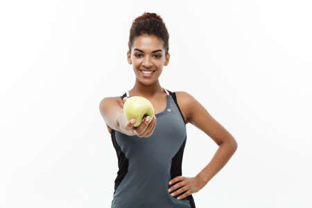 Healthy and Fitness concept - Beautiful American African lady in grey fitness clothes holding green apple. Isolated on white background.の写真素材