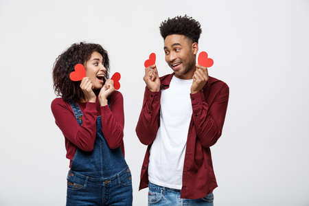 Beautiful Afro American couple holding two red paper heart, looking at camera and smiling, isolated on white backgroundの写真素材