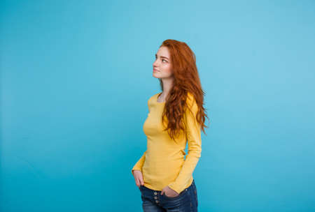 Lifestyle concept - Close up Portrait young beautiful attractive ginger red hair girl playing with her hair with shyness. Blue Pastel Background. Copy spaceの写真素材