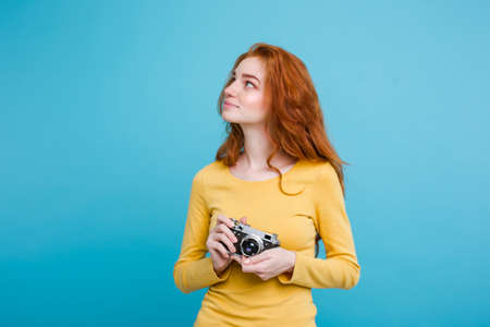 Travel concept - Close up Portrait young beautiful attractive redhair girl wtih trendy hat ,sunglass and vintage camera smiling to camera. Blue Pastel Background. Copy spaceの写真素材