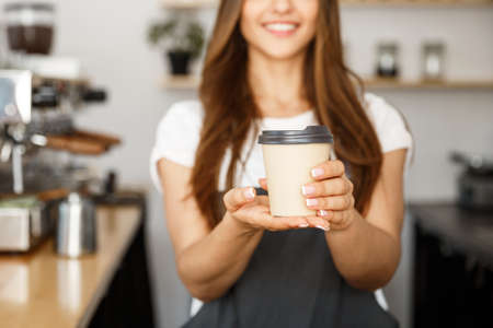 Coffee Business Concept - Beautiful Caucasian lady smiling at camera offers disposable take away hot coffee at the modern coffee shopの写真素材