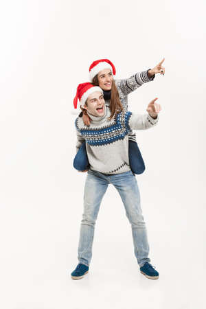Christmas Concept - Full-length Young happy couple in sweaters enjoying piggyback ride isolated on white grey backgroundの写真素材