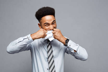 Business Concept - Young angry African American businessman while eating balled report paper. Unsuccessful Project.の写真素材