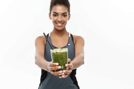 Healthy and Fitness concept - Beautiful American African lady in fitness clothing drinking healthy vegetable drink. Isolated on white background.の写真素材