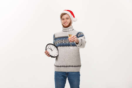 Holiday concept - Young handsome beard man in sweater with white clock and champagne over white studio background.の写真素材