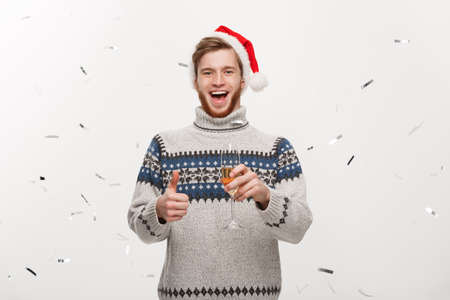 Chirstmas Concept - Happy young caucasian beard man holding champagne glass with confetti background celebrating for Christmas day.の写真素材