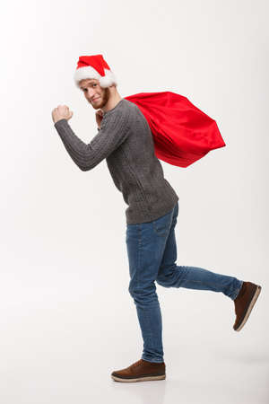 Christmas concept - Young confident beard man running and holding red big santa bag with a lot of present inside.の写真素材