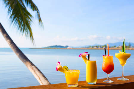 Smoothies and cocktail mango drinks with straw and mint in a glass beaker. A tropical fruit. on Wooden desk and tropical coconut background.の写真素材