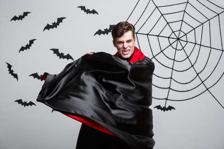 Vampire Halloween Concept - Portrait of handsome caucasian Vampire halloween costume fluttering his red, black cloak.の写真素材