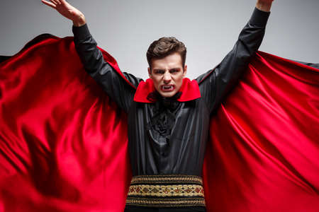 Vampire Halloween Concept - Portrait of handsome caucasian Vampire halloween costume fluttering his red, black cloak.の写真素材