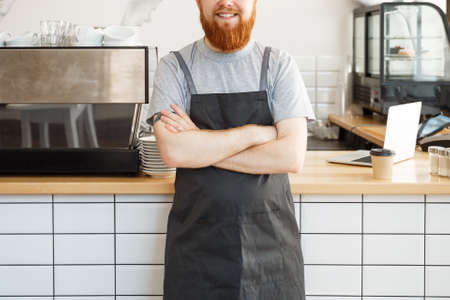 Coffee Business owner Concept - Portrait of happy young bearded caucasian barista in apron with confident looking and smiling to camera in coffee shop counterの写真素材