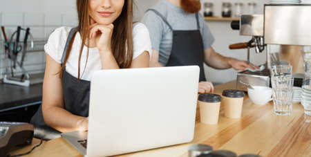 Coffee Business Concept - beautiful caucasian bartender barista or manager working and planing in laptop at modern coffee shop.の写真素材