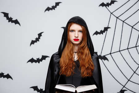 Halloween Concept - Beautiful dark priest casting spell with magic book on grey background.の写真素材