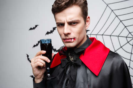 Vampire Halloween Concept - Portrait of Serious handsome caucasian Vampire enjoy drinking bloody red wine.の写真素材
