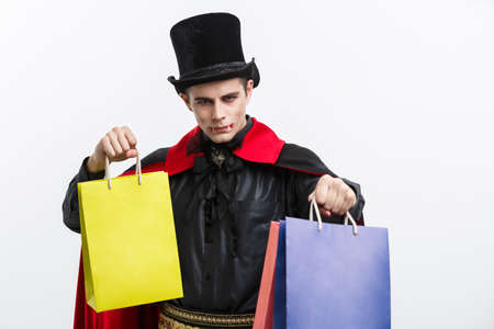 Vampire Halloween Concept - Happy handsome caucasian Vampire holding colorful shopping bag on white background.の写真素材