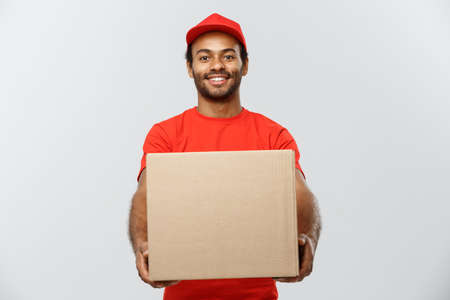 Delivery Concept - Portrait of Happy African American delivery man in red cloth holding a box package. Isolated on Grey studio Background. Copy Space.の写真素材