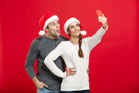 Christmas Concept - Young attractive couple taking a selfie by mobile phone celebrating in Christmas dayの写真素材