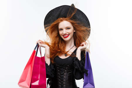 Halloween witch concept - Happy Halloween Witch smiling and holding colorful shopping bags on white background.の写真素材