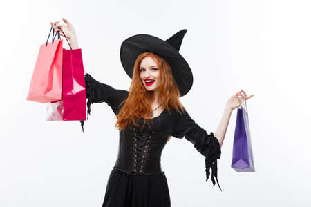 Halloween witch concept - Happy Halloween Witch smiling and holding colorful shopping bags on white background.の写真素材