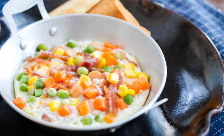 breakfast with fried eggs in a pan with bacon and vegetables on dark plateの写真素材