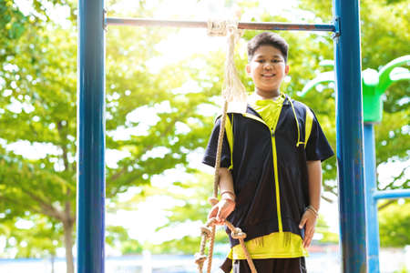 Young asian boy hang the yellow bar by his hand to exercise at out door playground under the big tree.の写真素材